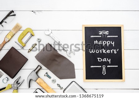 Happy Workers' Day background concept. Flat lay of construction blue collar handy tools and white collar's accessories over wooden background with black chalkboard and Happy Workers' Day text.