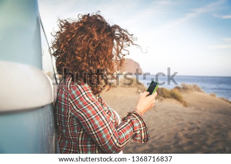 unrecognizable girl using cellphone seashore, leaning against vintage van, auburn curly hair ruffled wind, middle-aged woman vacation island chatting friends, concept light-heartedness relaxation