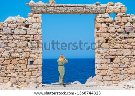 A girl is looking at the deep blue sea at Firopotamos village in  Milos, Greece through a window of the remains of an ancient building