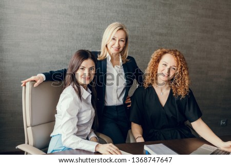 Portrait of three smiling beautiful female fashion designers of european ethnicity, working as a team, posing for photo against grey wall