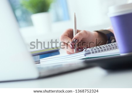 Businesswoman making notes with silver pen in office background. Just hands over the table. Business finance savings loan and credit concept.