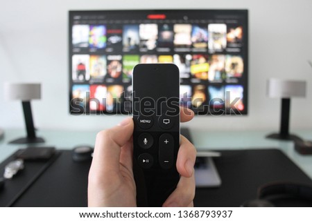 Hand holding a TV remote while watching shows on a streaming service on Television. Royalty-Free Stock Photo #1368793937