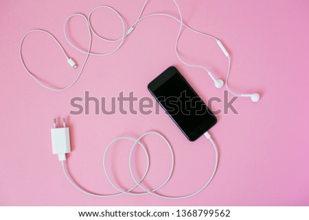 Top view of a smartphone with headphones and charge on trendy pink background.