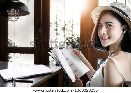 Portrait of young woman wearing hat holding book and looking at camera while sitting in cafe.