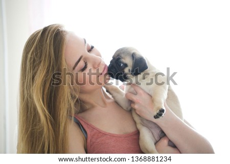 blonde girl with long hair kisses and holds a pug puppy in her arms, high key, gentle toning