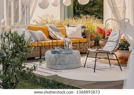 Real photo of an armchair, pouf as a table and wicker couch on a terrace