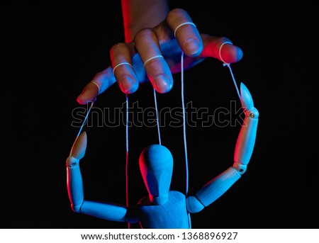 Concept of control. Marionette in human hand. Objects are colored on red and blue light. Royalty-Free Stock Photo #1368896927