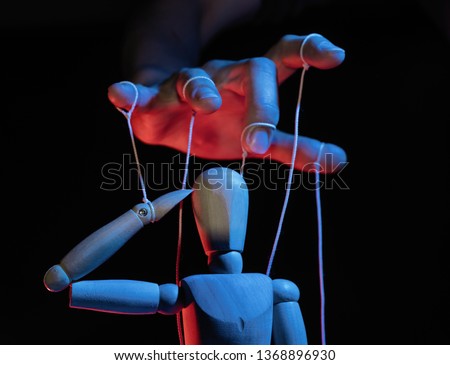 Concept of control. Marionette in human hand. Objects are colored on red and blue light. Royalty-Free Stock Photo #1368896930