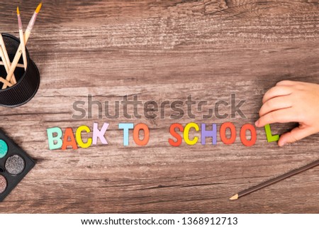 Top view flat lay boy hands play the alphabets toys on his vintage old wooden desk with notebook ,paint brush, colors painting, paper work and pencil with copy space, back to school background concept