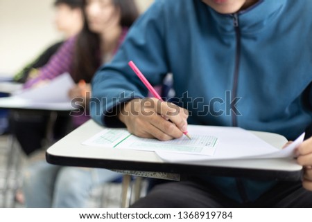 high school or university student holding pencil writing on paper answer sheet.sitting on lecture chair taking final exam attending in examination room or classroom.student in uniform  Royalty-Free Stock Photo #1368919784