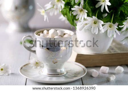 Coffee with marshmallows and a bouquet of anemone on a light background.