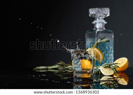 Cocktail gin-tonic with lemon slices and twigs of rosemary. Piece of ice falls into the glass. Copy space.