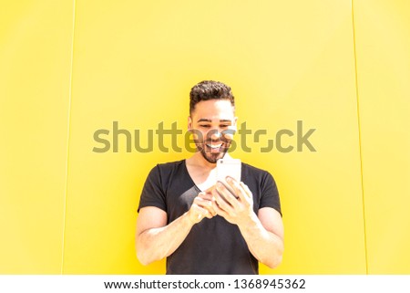 Young Man Using Mobile Phone Over a Yellow Wall Outdoors. Handsome Guy Taking a Selfie with His Cellphone and Smiling. Lifestyle Concept.