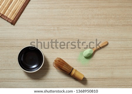 Powder organic matcha milk green tea in a spoon with bowl and bamboo whisk on wooden table, flat lay food, copy space for design