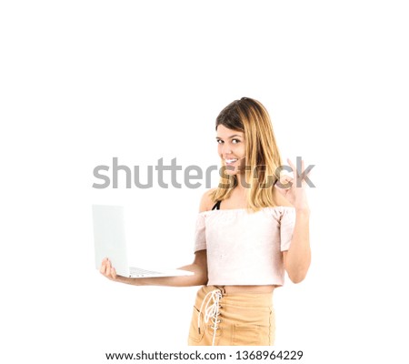 Beautiful blonde teenager girl doing an ok gesture with her hand while holding a laptop against a white background