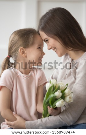 Vertical image small daughter and mom tender moment, family sitting together touching foreheads look at each other eyes celebrate eight march holiday, international womens day, happy birthday concept
