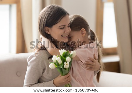 Overjoyed sisters embracing sitting on couch mother closed eyes enjoy pleasant moment adorable loving kid girl daughter congratulate on international women day make surprise white tulips concept image