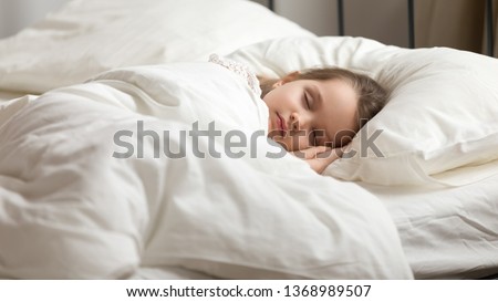 Calm adorable little daughter take day nap. Tranquil preschool child girl covered with white fresh duvet lying in bed comfortable mattress on bedroom. Healthy enough sleeping, zzz, good night, concept Royalty-Free Stock Photo #1368989507