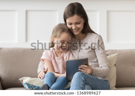 Mother cuddle daughter family sitting on couch in living room having fun using tablet computer watching cartoons online educational program. Modern wireless tech usage leisure at home with kid concept