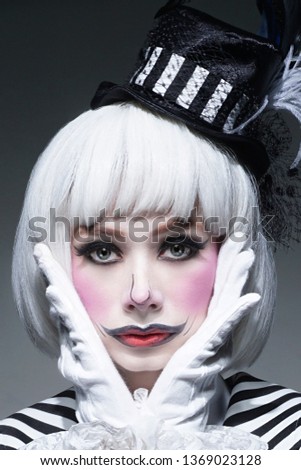 Sad clown make-up with uncombed white hair.Pensive woman in Halloween clown costume. Masquerade girl with vintage dress. Clown on gray background.