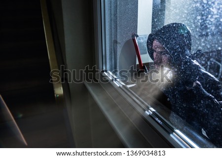 Burglar With Crowbar And Flashlight Looking Into A House Windows Royalty-Free Stock Photo #1369034813