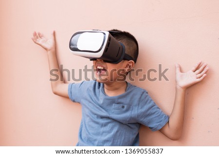 Asian boy experiencing and wearing virtual reality headset on pink wall background.A kid using VR glasses and funny time at home.A boy watching 3D in the movie box.