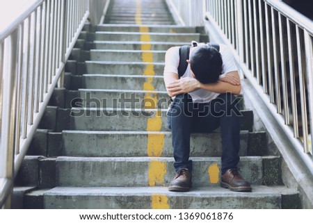 A young man who is suffering, disappointed, saddened, sitting on the stairs. Royalty-Free Stock Photo #1369061876