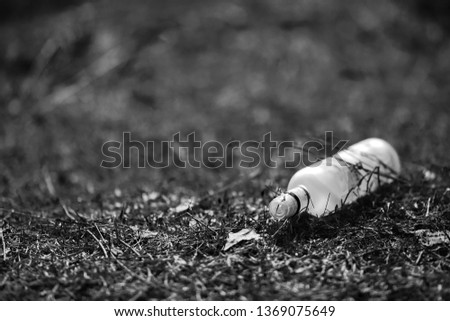 Empty white glass bottle lying on grass in early spring, polluted, conservancy. rubbish after last snows of winter black and white picture.