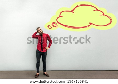 Full length portrait of handsome thoughtful bearded businessman in red shirt standing looking away and scratching his head and thinking with drawed cloud on wall. indoor studio shot on grey background