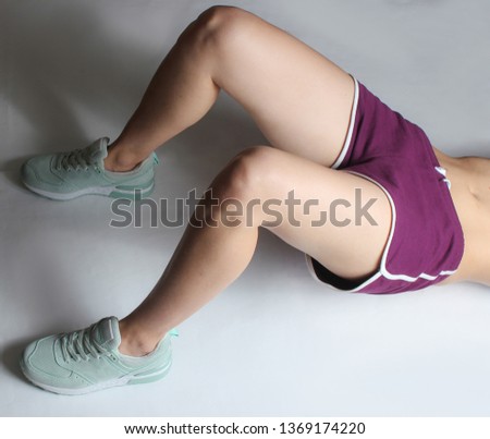 Cropped photo of sports female body in shorts and sneakers doing back ups exercise lying on white background