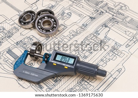 Micrometer screw gauge. Ball bearings. Drawing on background. Accurate measuring tool. Digital display. Round metal parts group. Engineering draft, plan, design. Education, study. Full depth of field.