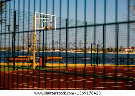 a sports field for playing basketball covered with a safety net is in a city park on the banks of the river.