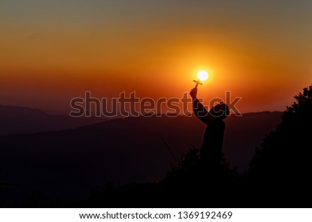 Silhouette of woman praying with cross in nature sunrise background.