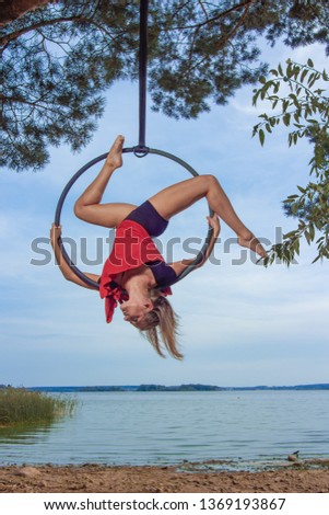gymnast girl aerial acrobatics on the ring on the background of the lake and the sky at sunset