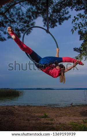 gymnast girl aerial acrobatics on the ring on the background of the lake and the sky at sunset