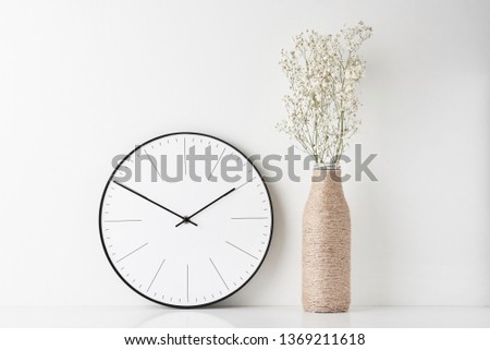 Front view desk with round wall clock and flower in bottle vase on white background. Home office minimal workspace desk