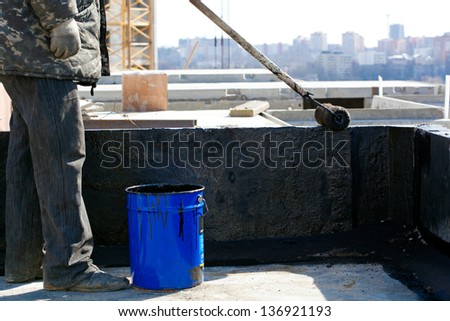 Roofer worker painting black coal tar or bitumen at concrete surface by the roller brush Royalty-Free Stock Photo #136921193