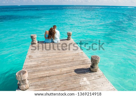 Couple siting at the wooden pier, hugging and looking at the turquoise water of caribbean sea in Cancun. Drone view picture.