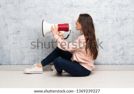 Teenager student girl studying in a table shouting through a megaphone