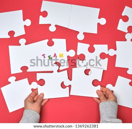 female hand puts white big puzzles on a red background,  inscription team. concept of recruitment in the company