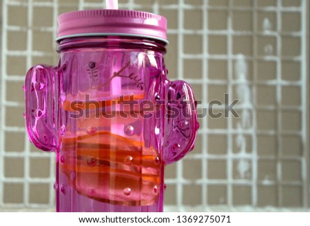 Pink glass of bank with a tube with water with addition of lemons and apples on a grey background, selective focus.
