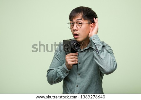 Young chinese man holding a vintage camera try to listening a gossip