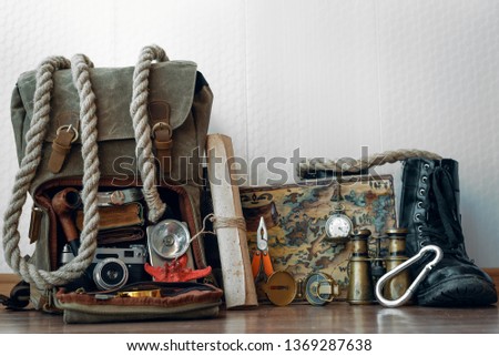 Travel or adventure background. Treasure map, backpack, boot, binoculars, compass, pocket watch, rope and photo camera on a floor on a white wall background .