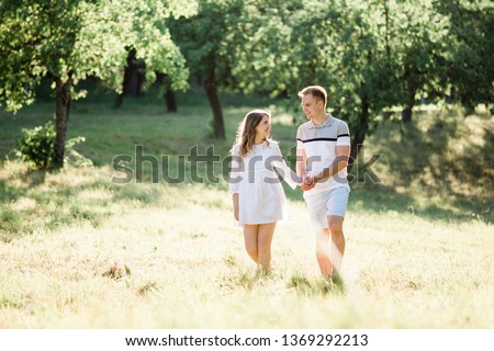 Young pretty couple in love walking  in park. Handsome cheerful blonde girl in white dress hugging her boyfriend. Man and woman having fun outdoors