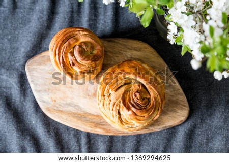 Two different size cruffins( or Easter breads) on wooden board with blooming cherry branches in glass jar on dark background.