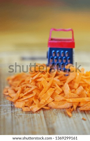 A small grater and a large carrot on a cutting board, in the kitchen. Optical illusion. Close-up. Shallow depth of field. Vertical image                           
