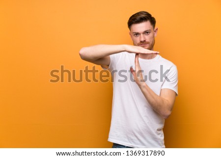 Redhead man over brown wall making time out gesture
