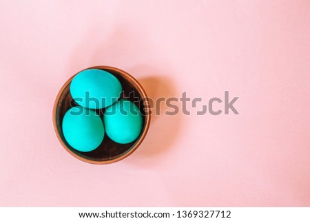 Three Easter eggs of turquoise color in a wooden plate on a soft pink background. Trend of the year.