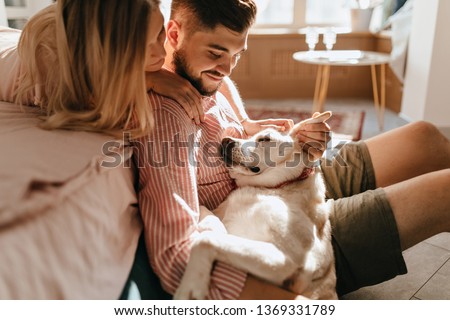 Dog lies on legs of owner. Man in pink shirt and his beloved woman admire their white pet Royalty-Free Stock Photo #1369331789