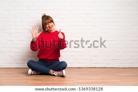 Redhead woman siting on the floor counting six with fingers